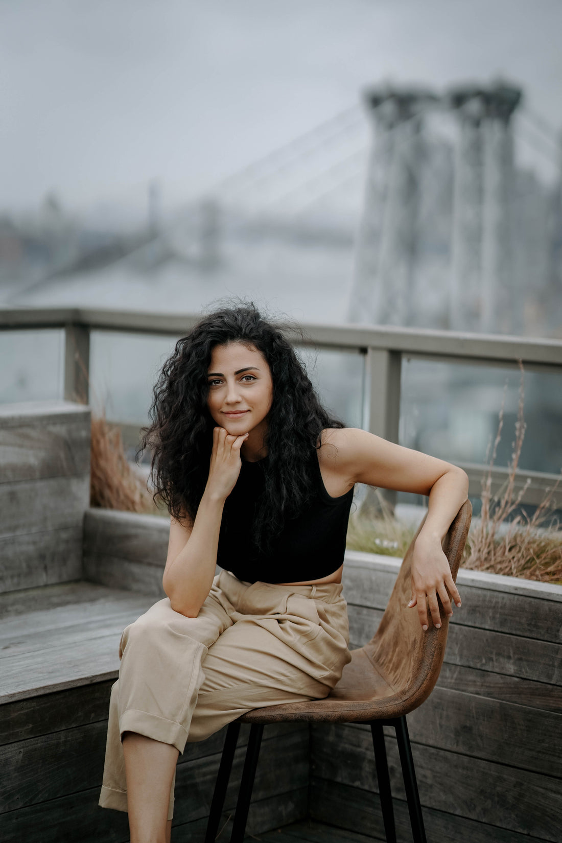 Vanessa is looking at the camera, standing on a rooftop in Williamsburg, New York. The Williamsburg bridge and Manhattan skyline are visible in the background.